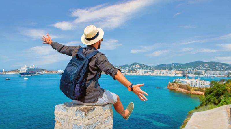 male standing on a mountain top looking out to sea with arms out